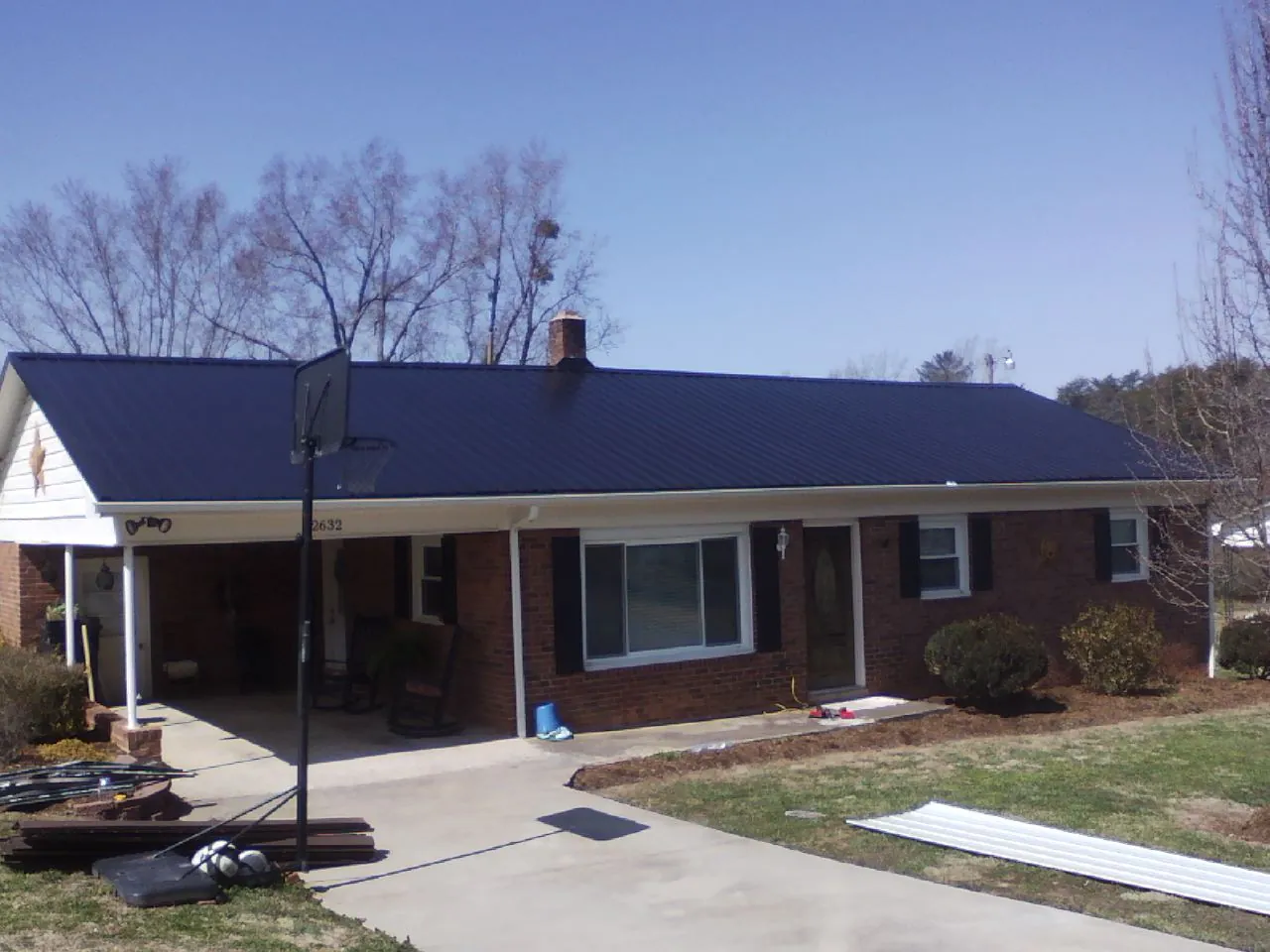 Finished dark blue metal roof on a brick ranch with a carport in Liberty