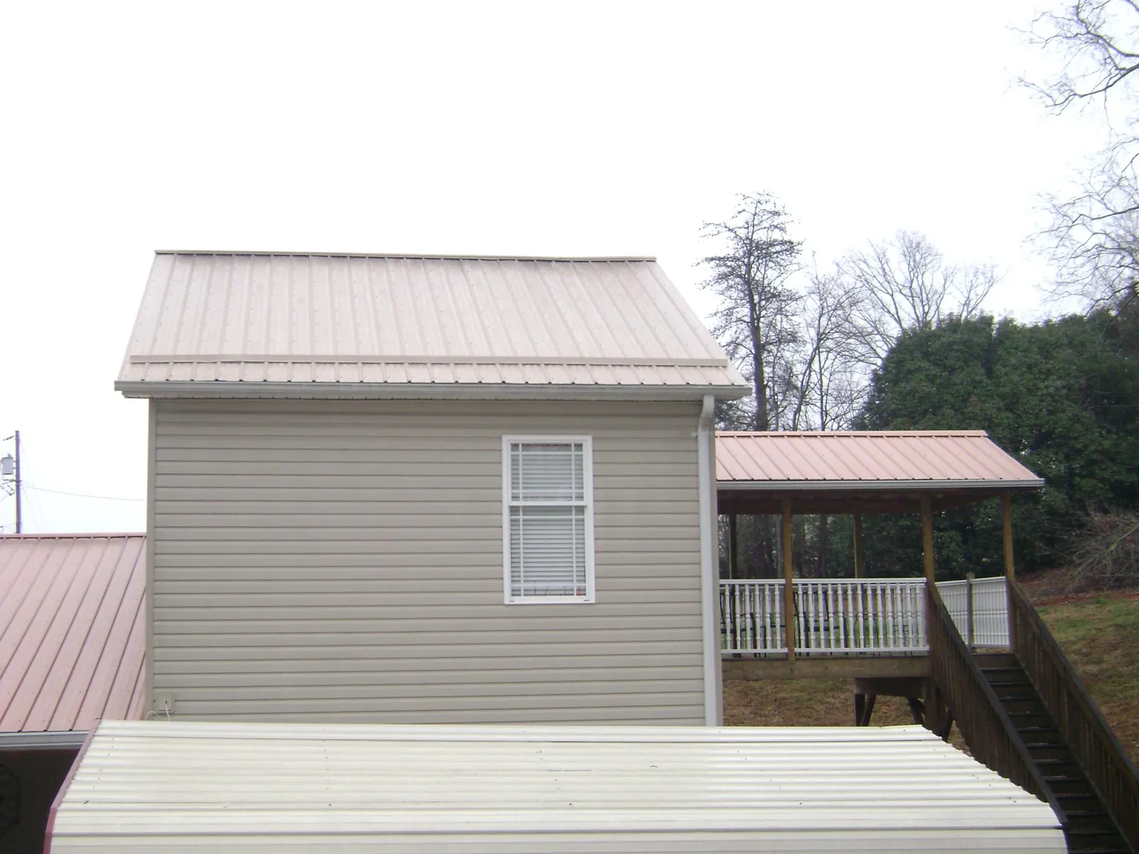 Tan metal roofs on a two story addition and attached porch, from a Roof Replacement job in Liberty